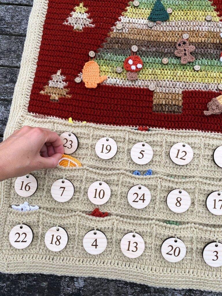 A hand a shown taking a small crochet decoration out of a pocket on an advent calendar ready to hang on the tree above