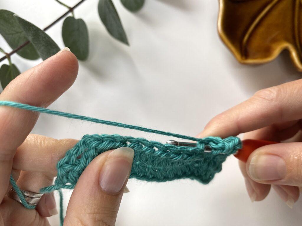 2 hands holding yarn and hook making an extended half double crochet stitch