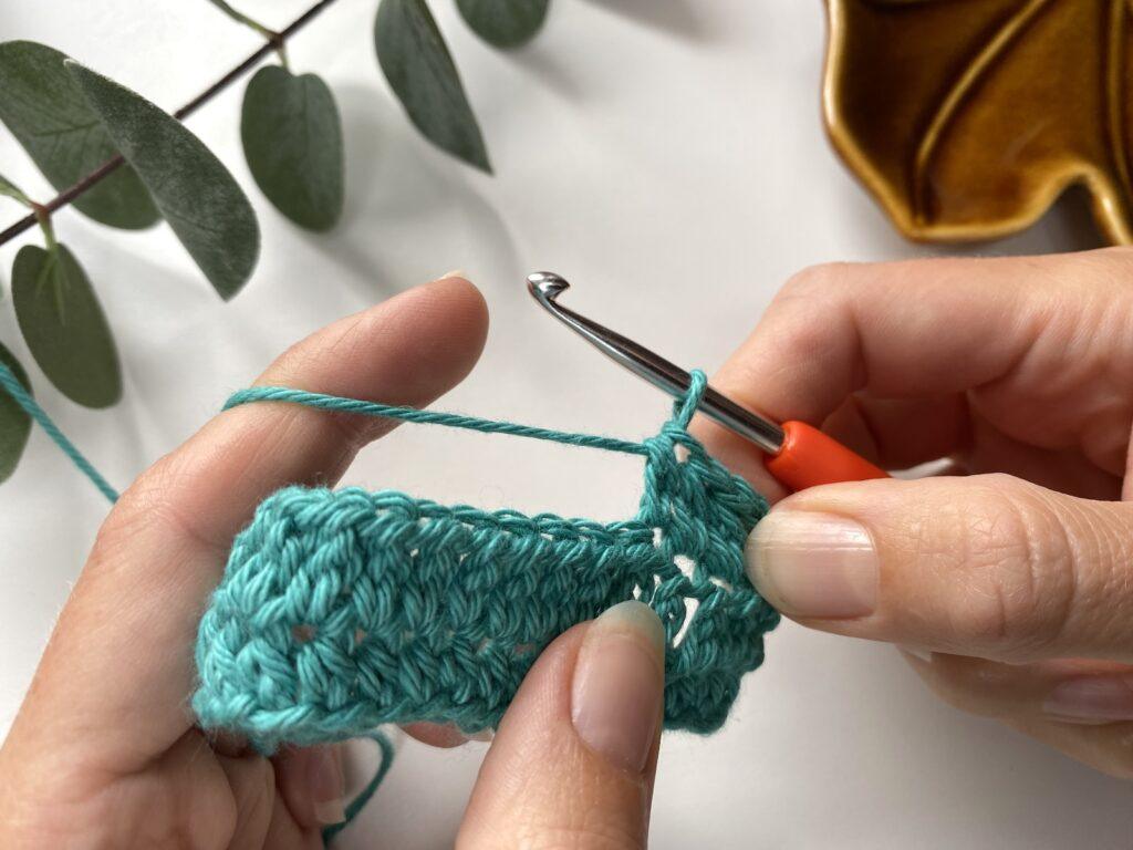 A person holding a crochet sample showing a completed extended half double crochet stitch