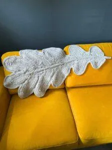 A giant crochet oak leaf in grey is draped over the back of a yellow sofa