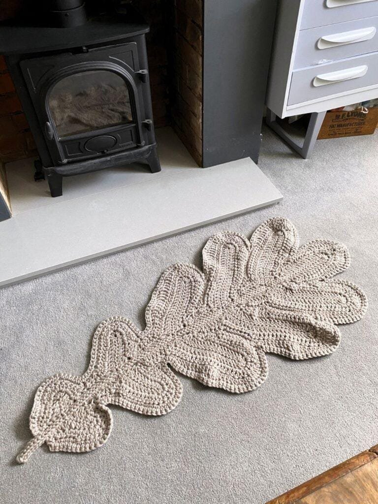 A crochet leaf blanket lays on the flor in front of the fireplace and a set of grey drawers