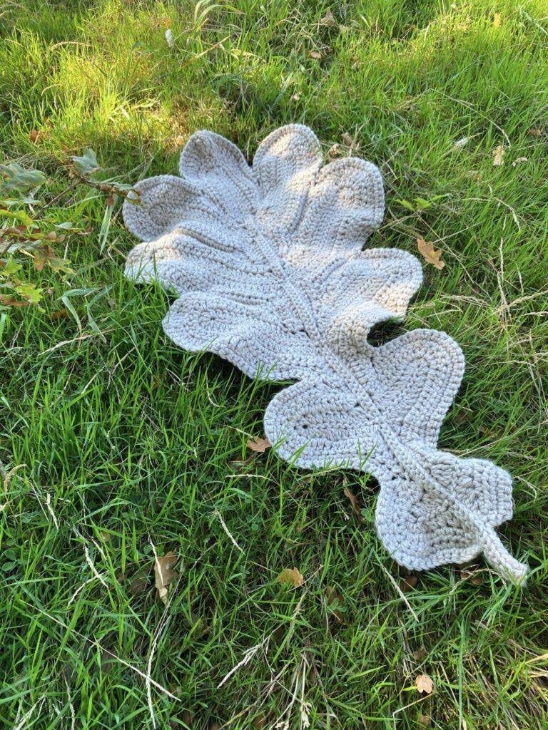 A giant crochet oak leaf is lain out on the grass in the autumn sunshine