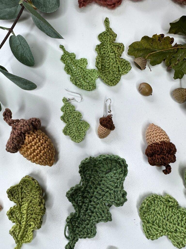 A flatlay of crochet acorn and oak leaf earrings along with other sized crochet acorns and leaves