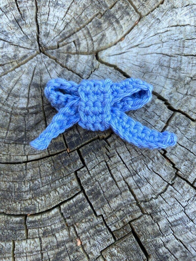 A blue crochet bow ornament lays on a wooden slice