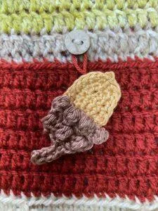 A crochet acorn is hanging on a red crochet background for a advent calendar