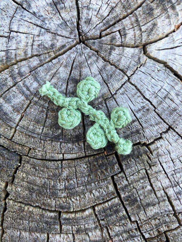 A set of small crochet eucalyptus leaves on a wooden slice