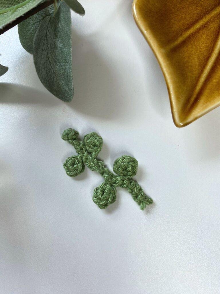 A tiny crochet leaf decoration with other leaves and a pottery leaf around