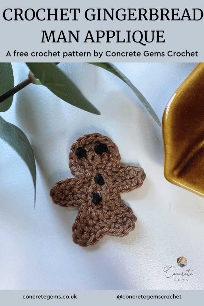 A crochet gingerbread man lay on a white surface with greenery and a pointed brown dish surrounding and the words CROCHET GINGERBREAD MAN APPLIQUE above