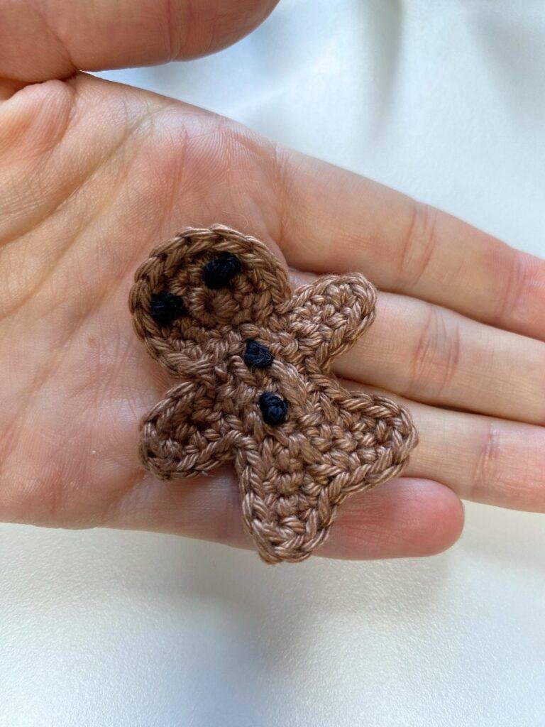 A hand holds a tiny crochet gingerbread man