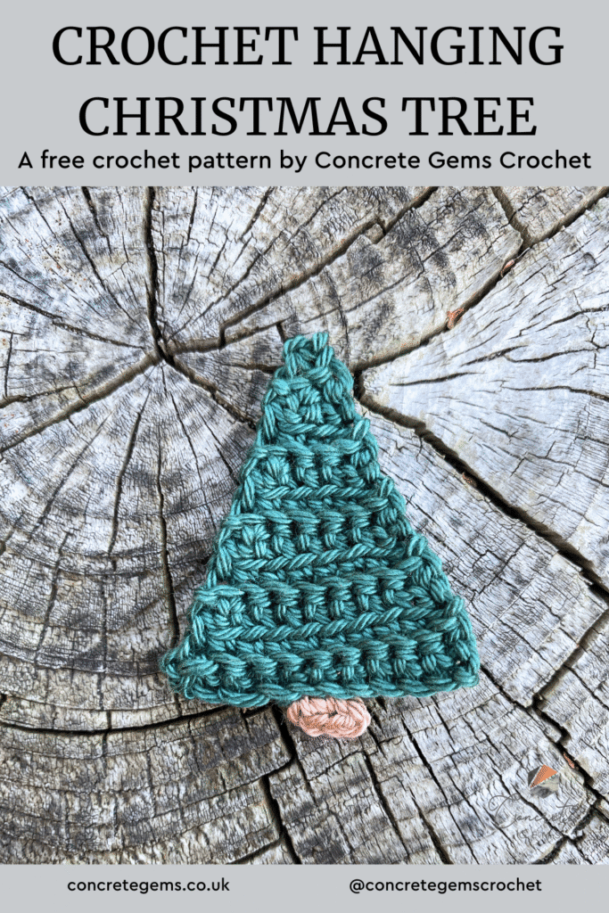 A green crochet Christmas tree is laid against a wooden slice