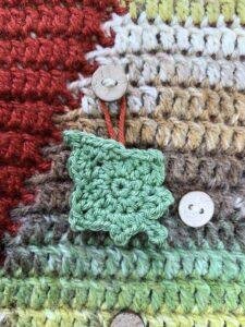 A green hanging crochet ivy leaf having on a Christmas tree crochet advent calendar background