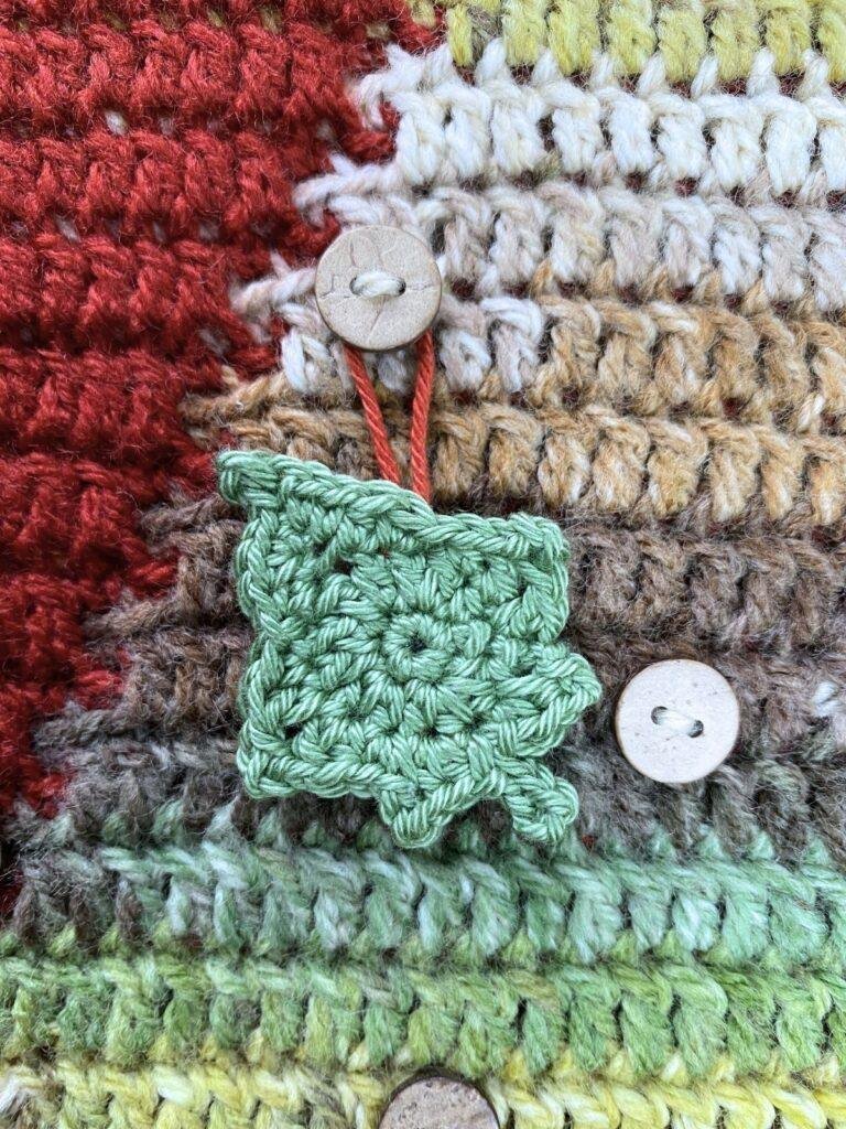 A green hanging crochet ivy leaf having on a Christmas tree crochet advent calendar background