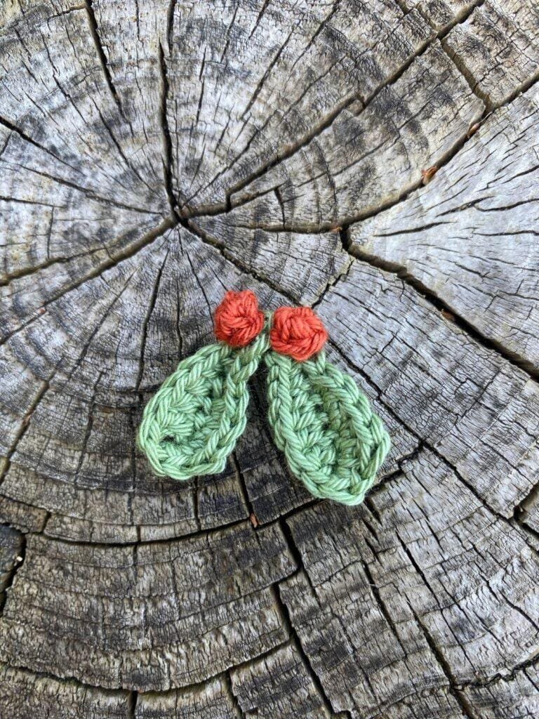 A crochet mistletoe and berries sits on a log slice
