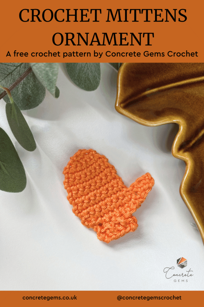 A flat orange crochet mitten decoration lies on a white background with leaves and a brown dish around the edge