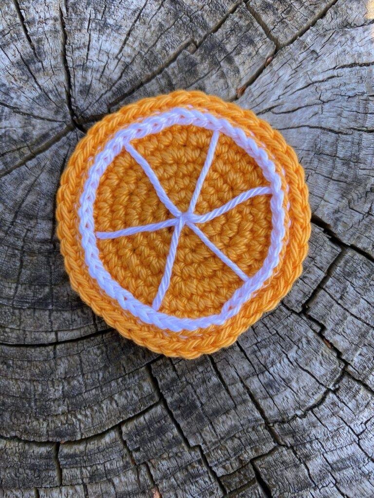 A crochet orange slice lays on a wooden surface