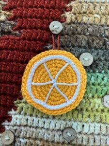 A crochet orange slice is hanging on a button on a crochet advent calendar