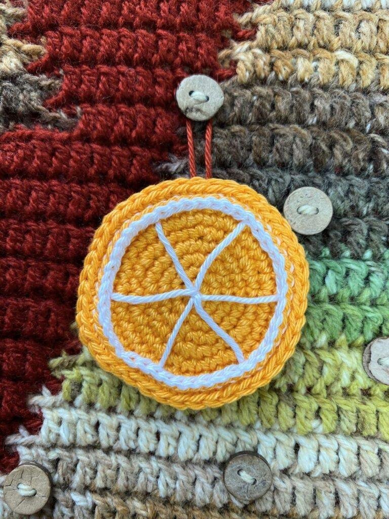 A crochet orange slice is hanging on a button on a crochet advent calendar