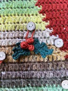 tiny crochet holly and berries hang on a crochet Christmas tree backdrop