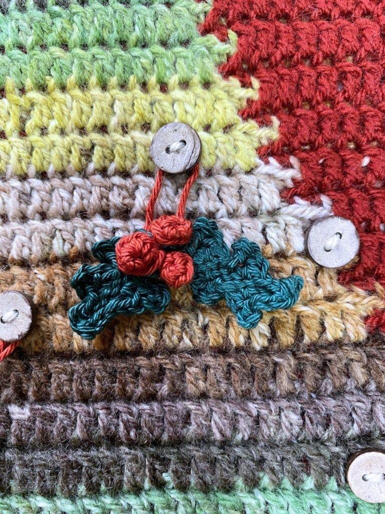 tiny crochet holly and berries hang on a crochet Christmas tree backdrop