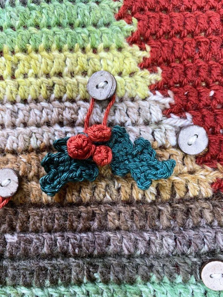 tiny crochet holly and berries hang on a crochet Christmas tree backdrop