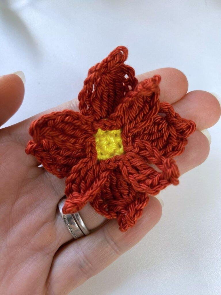A hand is holding a crochet poinsettia flower ornament