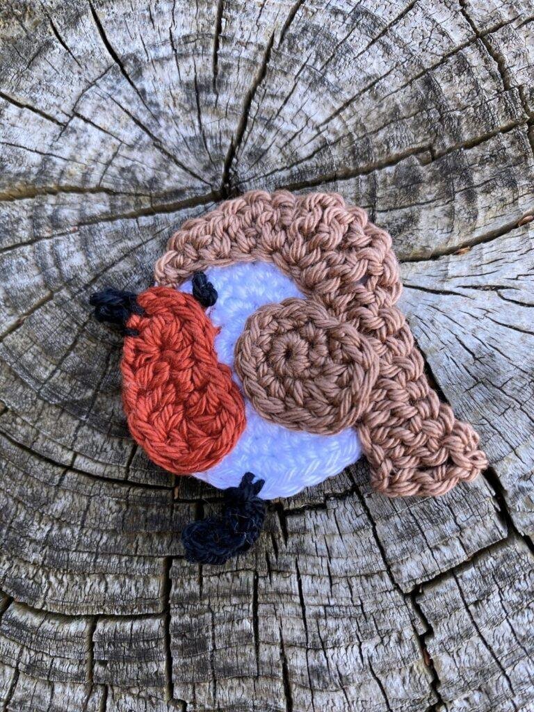 A flat crochet robin applique lays on a wooden slice