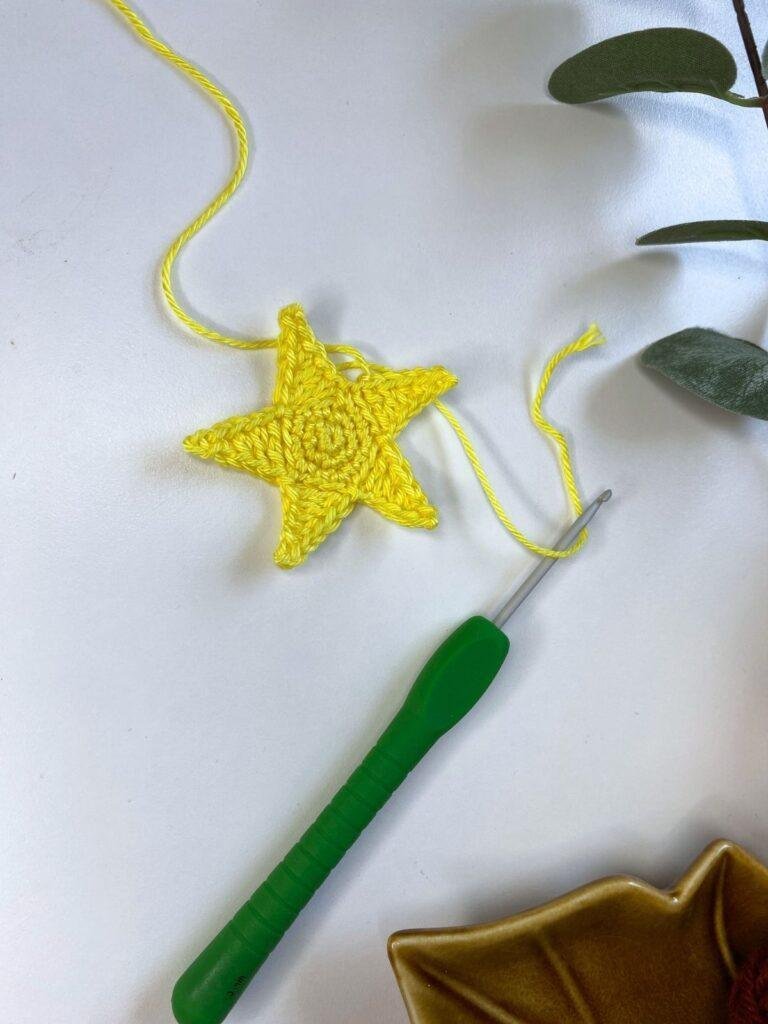 A crochet star being made with yellow yarn and a green hook