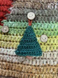 A small crochet Christmas tree decoration hangs on a button on a larger crochet background