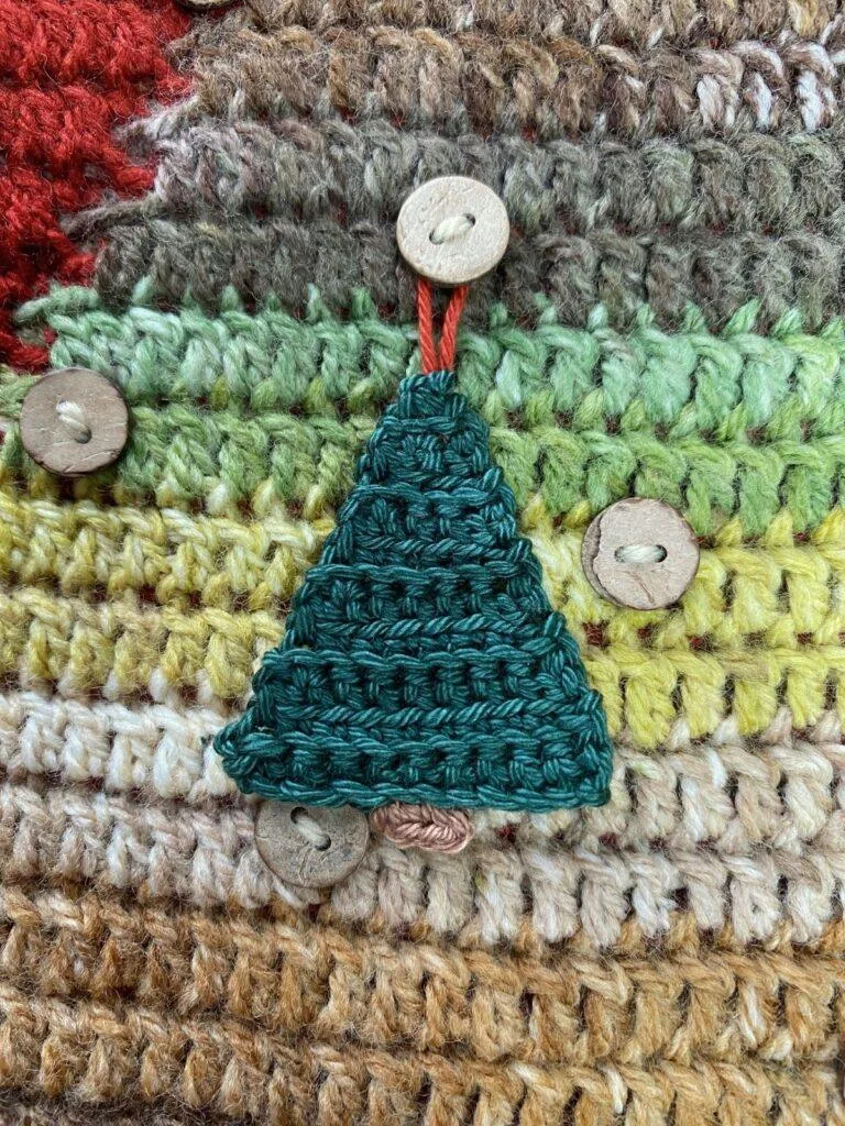 A small crochet Christmas tree decoration hangs on a button on a larger crochet background