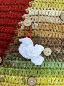 A small crochet dove is hanging on a button on a red, green and down crochet wall hanging