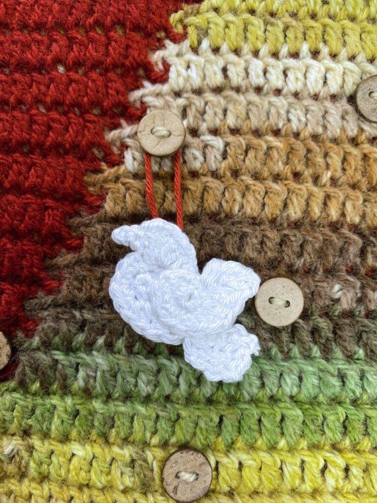 A small crochet dove is hanging on a button on a red, green and down crochet wall hanging