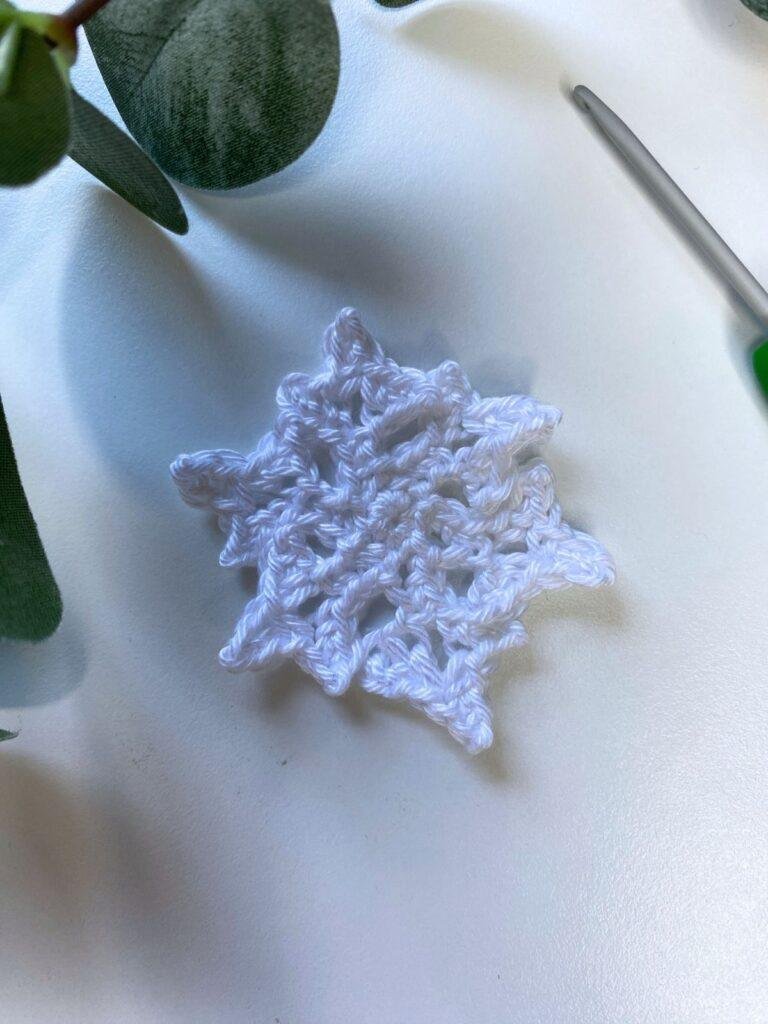 A crochet snowflake on a white background with green leaves and a crochet