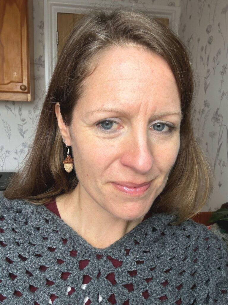 A woman in a grey crochet sweater wears tiny crochet acorn earrings 