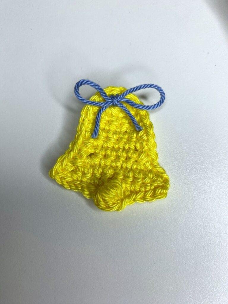 A crochet bell with a tiny ribbon lays on a white surface