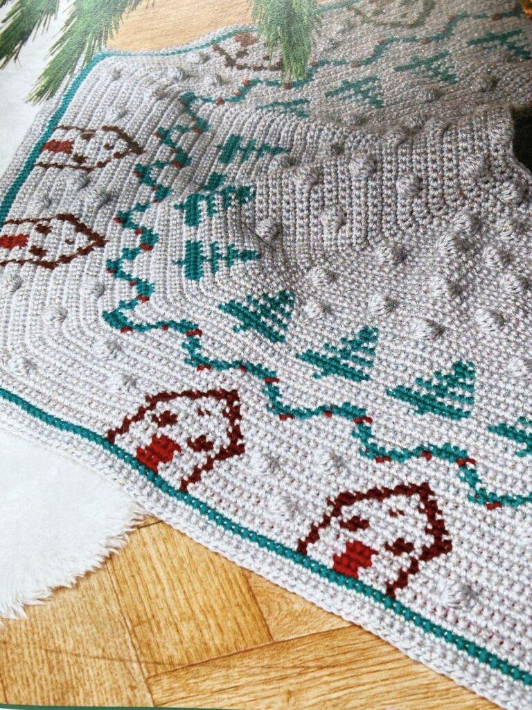 Close up of a crochet hexagonal blanket in silver with trees and houses on it.