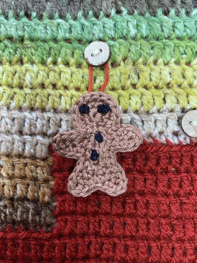 A tiny gingerbread man applique hangs on a button on a green and red crochet background