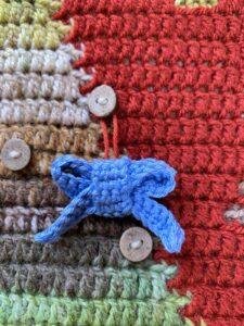 A tiny crochet blue bow is hanging from a button on a crochet advent calendar
