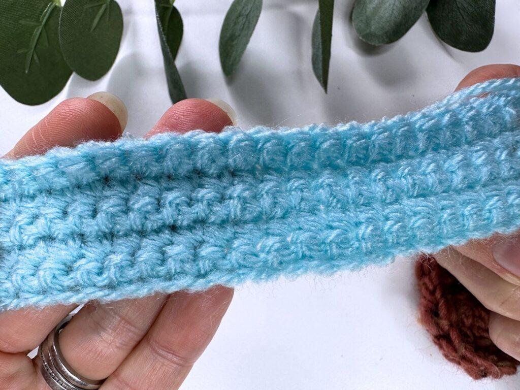 2 hands hold a small crocheted blue fabric, showing the single crochet stitch
