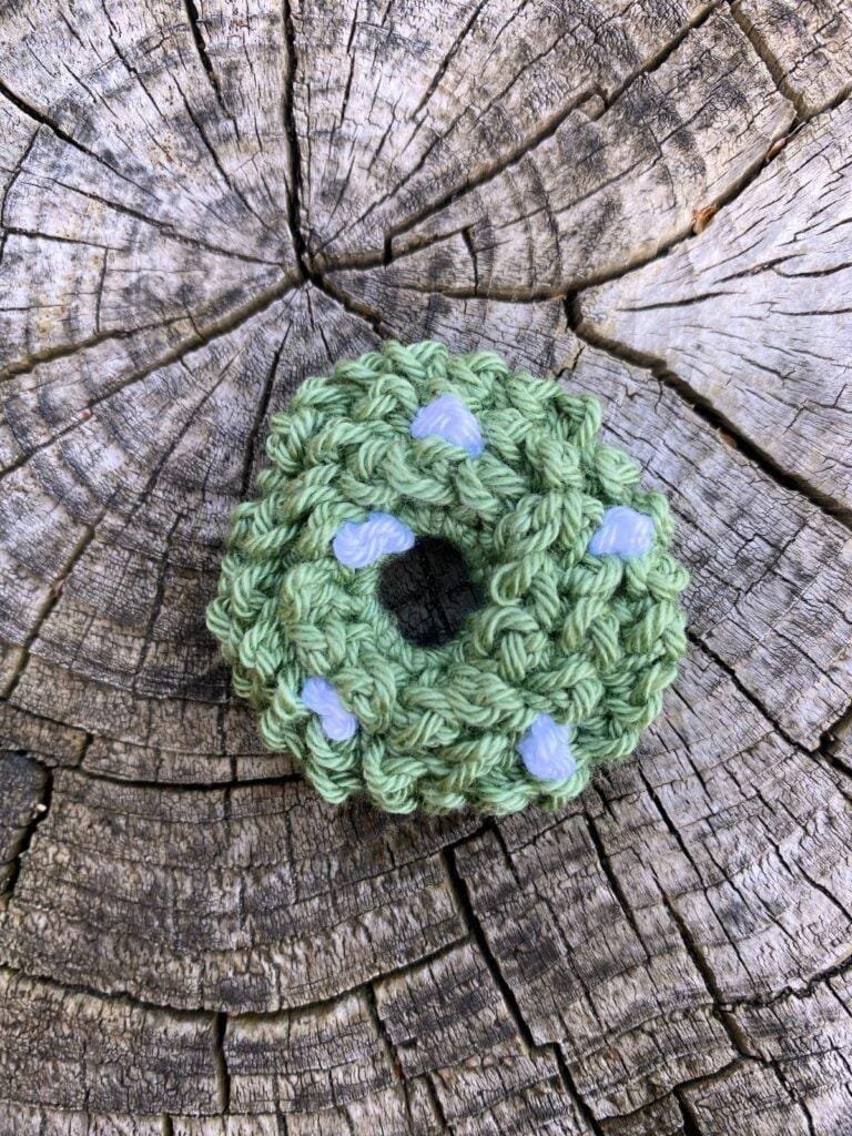 A small crochet wreath with white berries sits on a wooden slice