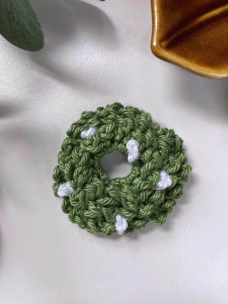 A small tree crochet Christmas wreath with white berries on is in the centre with a leaf and brown dish at the top