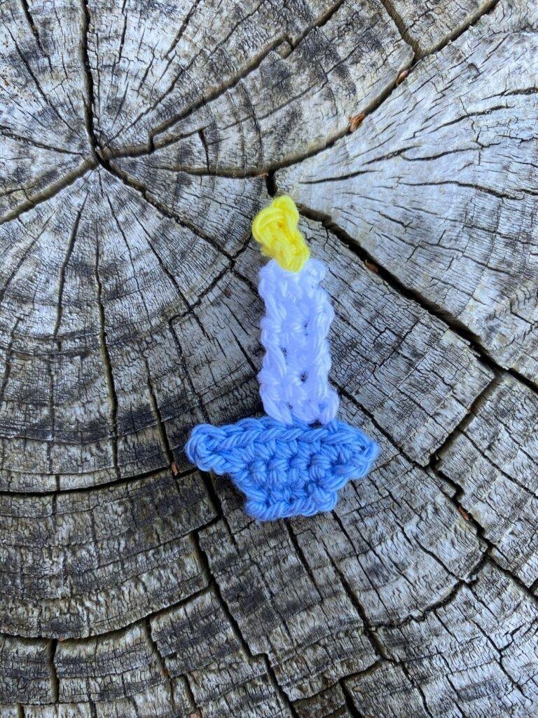 A small crochet candle with a blue holder lays on a wooden slice