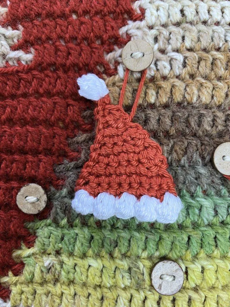 A tiny crochet Santa Hat hangs on a button on a crochet advent calendar