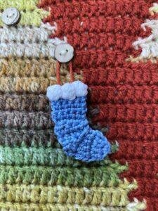 A mini blue crochet stocking ornament hangs on a button and a crochet Christmas tree