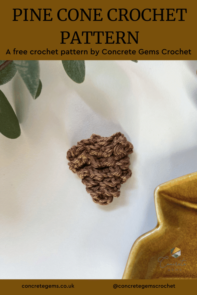 A brown crochet pine cone on a white surface with greenery and brown ceramic in the corners and the words PINE CONE CROCHET PATTERN above