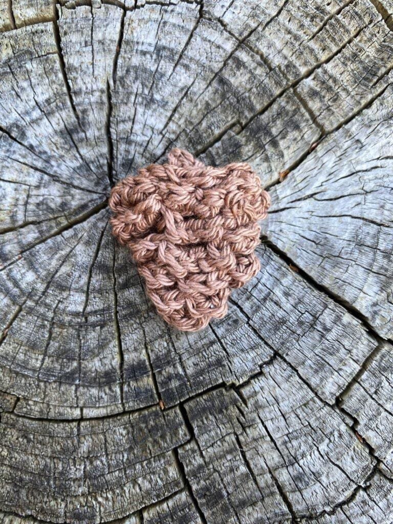 A crochet pinecone sits on a wooden slice