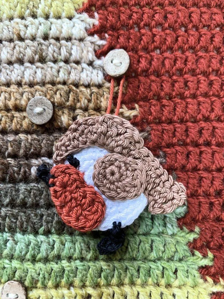 A cute round crochet robin hangs on a button on a crochet advent calendar