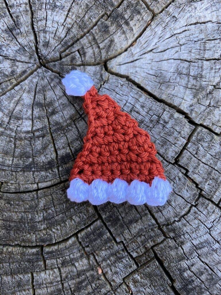 A small crochet Santa Hat lays on a wooden slice