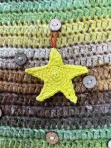 A yellow crochet star is hanging on a brown and green crocheted background