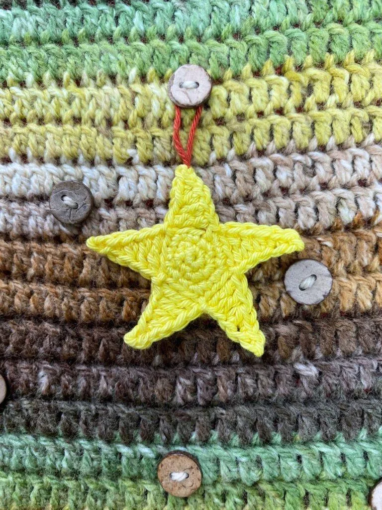 A yellow crochet star is hanging on a brown and green crocheted background