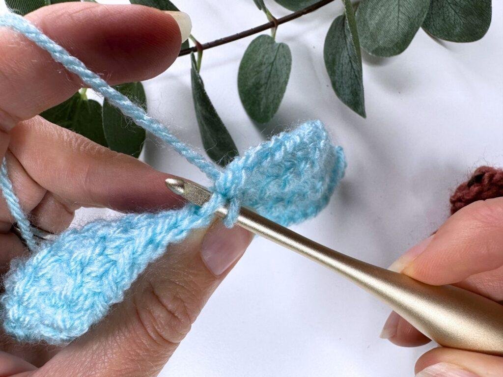 A crochet hook is inserted through the front loop of a crochet stitch in a piece of blue fabric